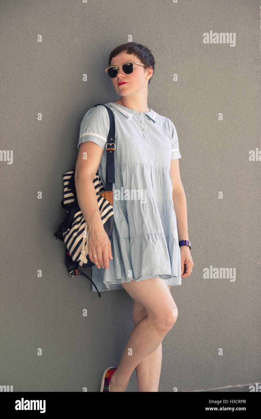 Mujer joven blogger de moda posando ropa casual simple pared gris Foto de stock