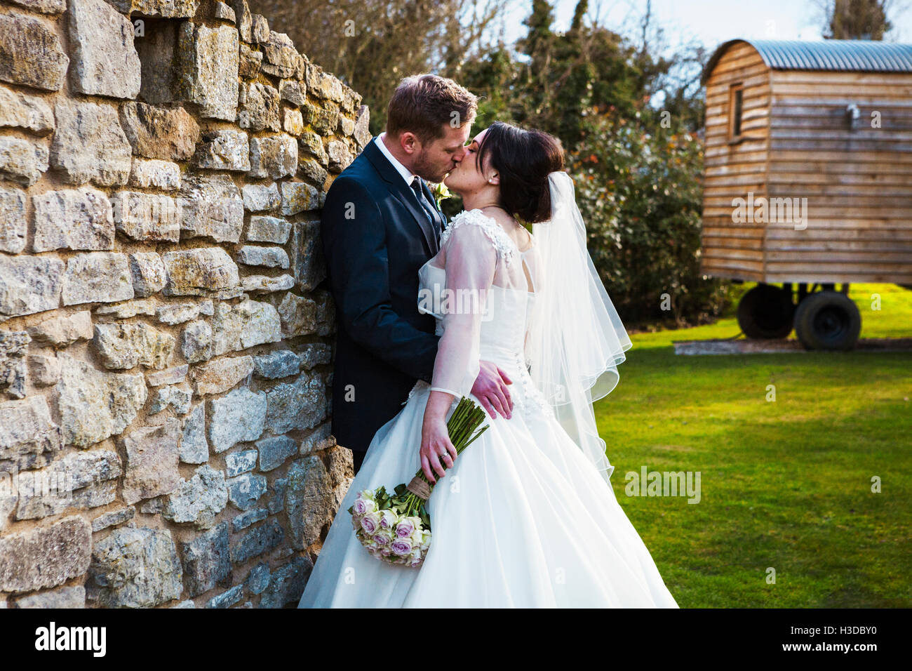 La novia y el novio besarse en su día de la boda de pie en un jardín. Foto de stock