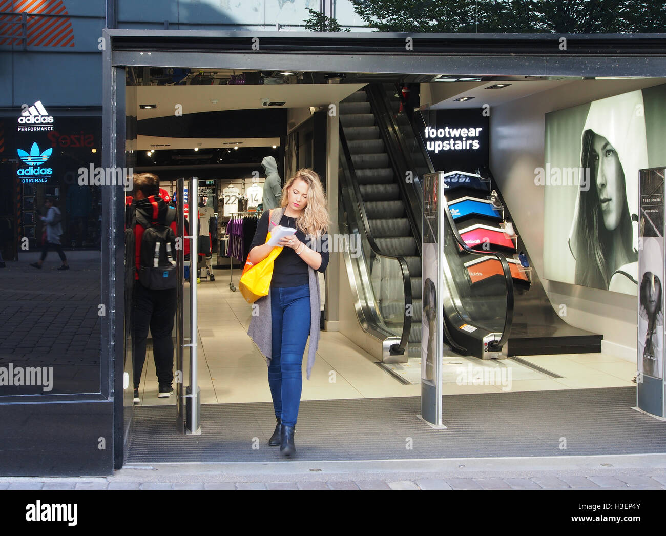 Tienda de ropa deportiva de Adidas en el de Manchester, Inglaterra, Reino Unido, con una joven mujer caucásica que sale de la tienda y hacer notas Fotografía de stock -
