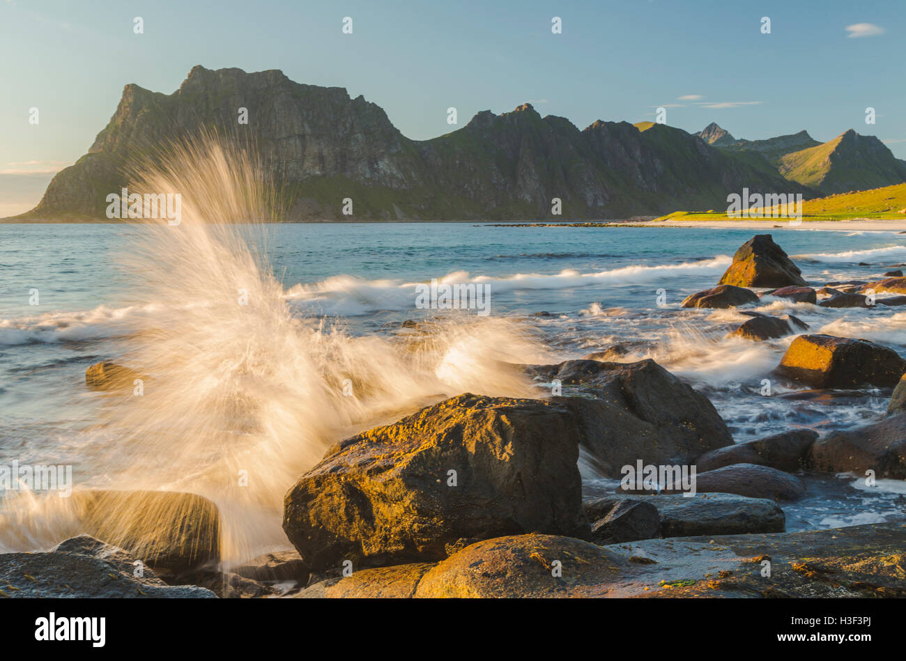 Rocas en luz del atardecer con una cálida luz brilla sobre ellos, olas rompiendo en la orilla y las salpicaduras de agua en las rocas, Uttakleiv, Lofote Foto de stock