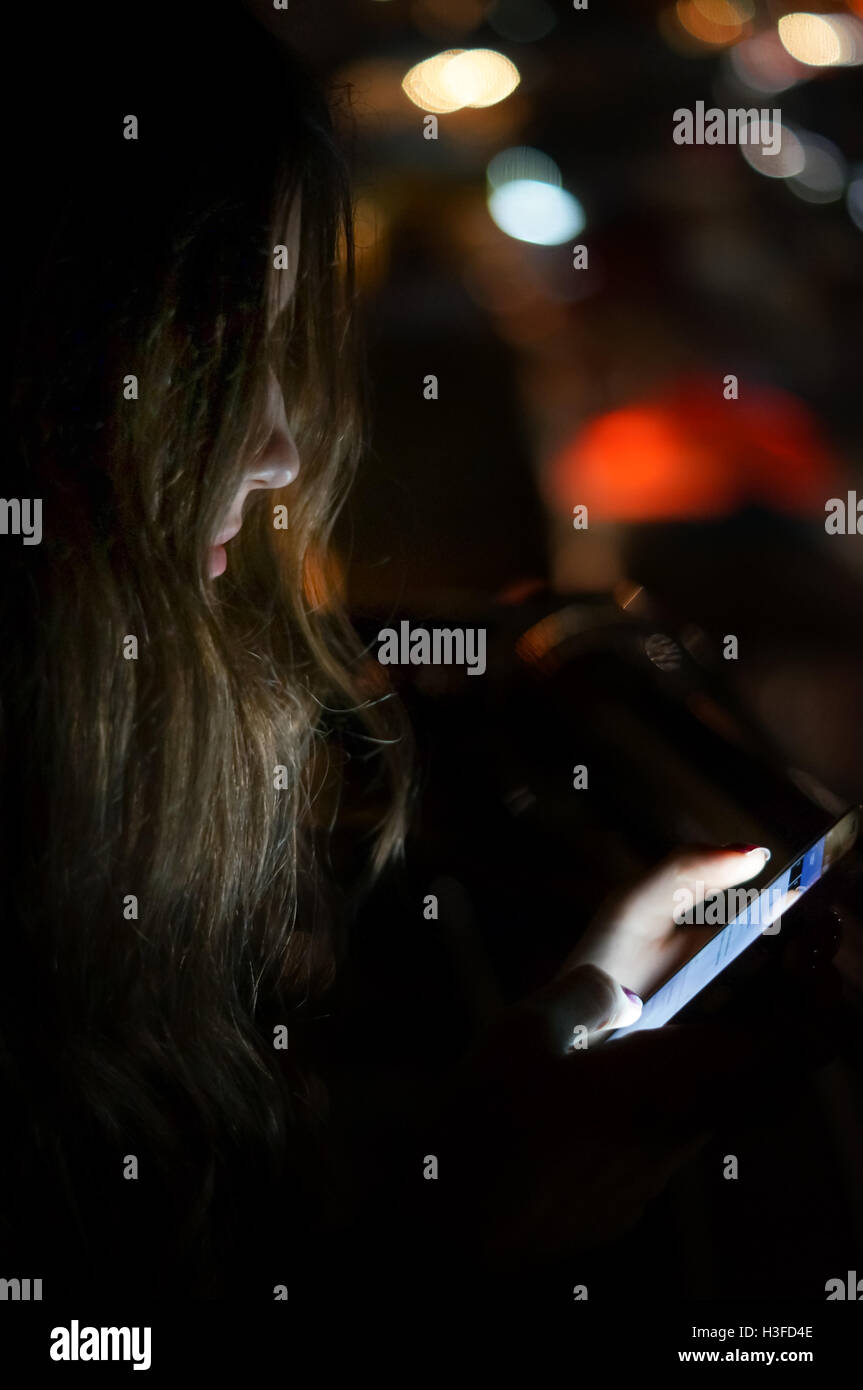 Chica utilizando smart phone en la noche delante de las luces de la ciudad borrosa Foto de stock