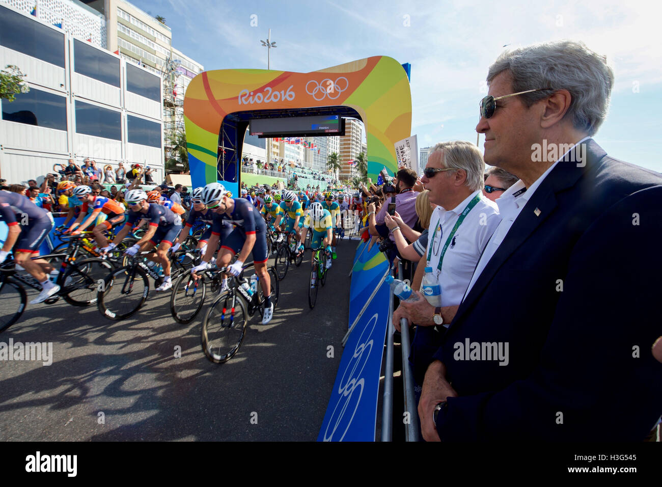 El Secretario de Estado de Estados Unidos, John Kerry relojes el inicio de los Juegos Olímpicos del hombre a lo largo de la carrera de ciclismo Copacobana playa en Río de Janeiro, Brasil, como él y sus colegas de la delegación presidencial de EE.UU. asistir a los Juegos Olímpicos de Verano el 6 de agosto de 2016. Foto de stock