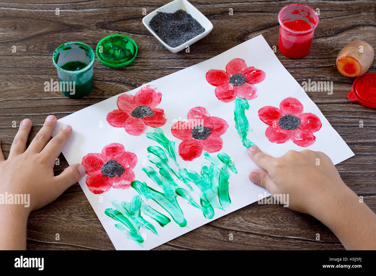 Dibujo sobre papel amapolas, hijo dibuja dedos hierba. Pegamento, pintura,  papel y patatas en una mesa de madera. Proyecto de arte para niños  Fotografía de stock - Alamy