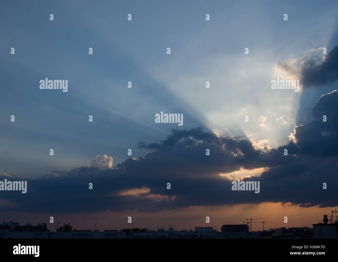Atardecer nublado con rayos crepusculares en las azoteas de la ciudad Foto de stock