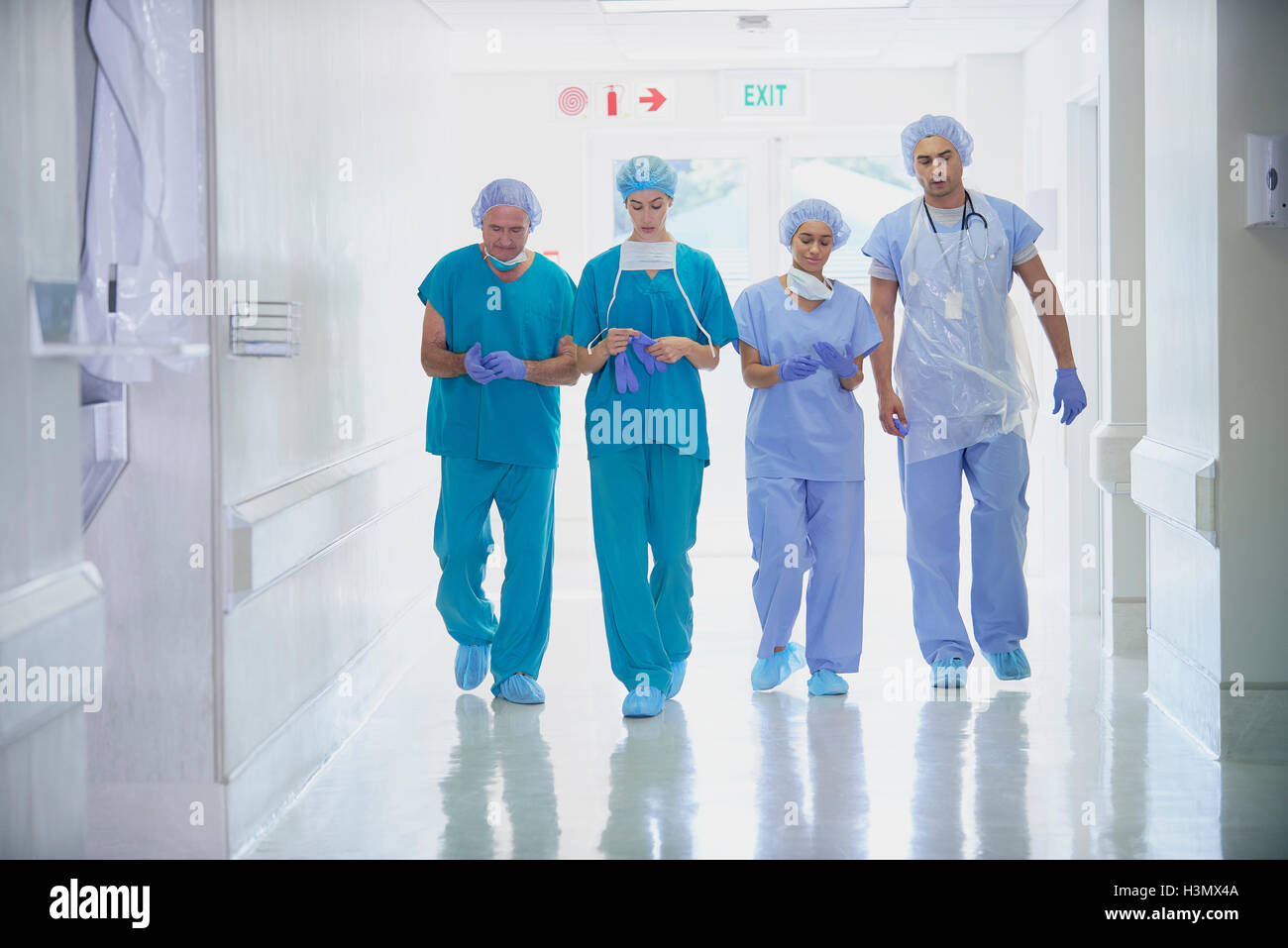 Cuatro funcionarios médicos vistiendo scrubs caminando en el pasillo del hospital Foto de stock