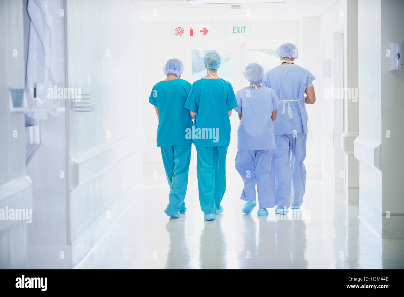 Vista trasera de cuatro funcionarios médicos vistiendo scrubs caminando en el corredor del hospital Foto de stock