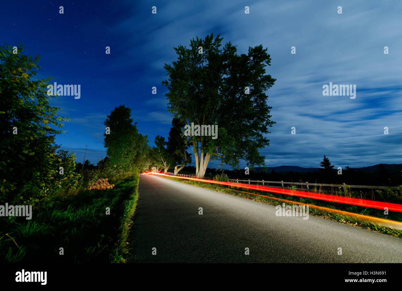 Alquiler de faros y luces de cola desplazándose hacia abajo por un carril del país por la noche Foto de stock