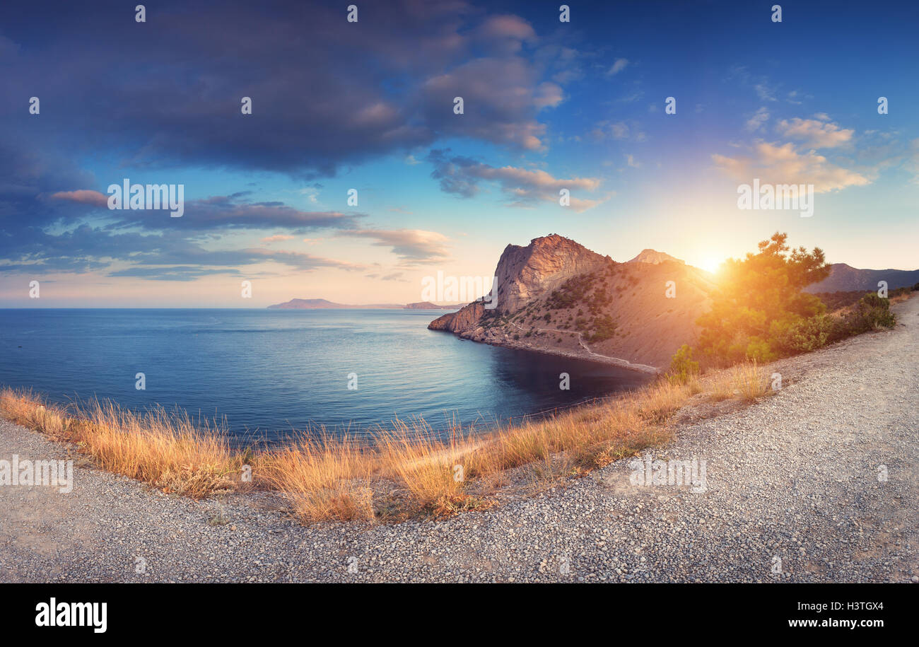 Colorido paisaje de montaña con PATH, hierba amarilla, el mar, el cielo azul y bellas nubes al atardecer en la Crimea. Verano en las montañas Foto de stock