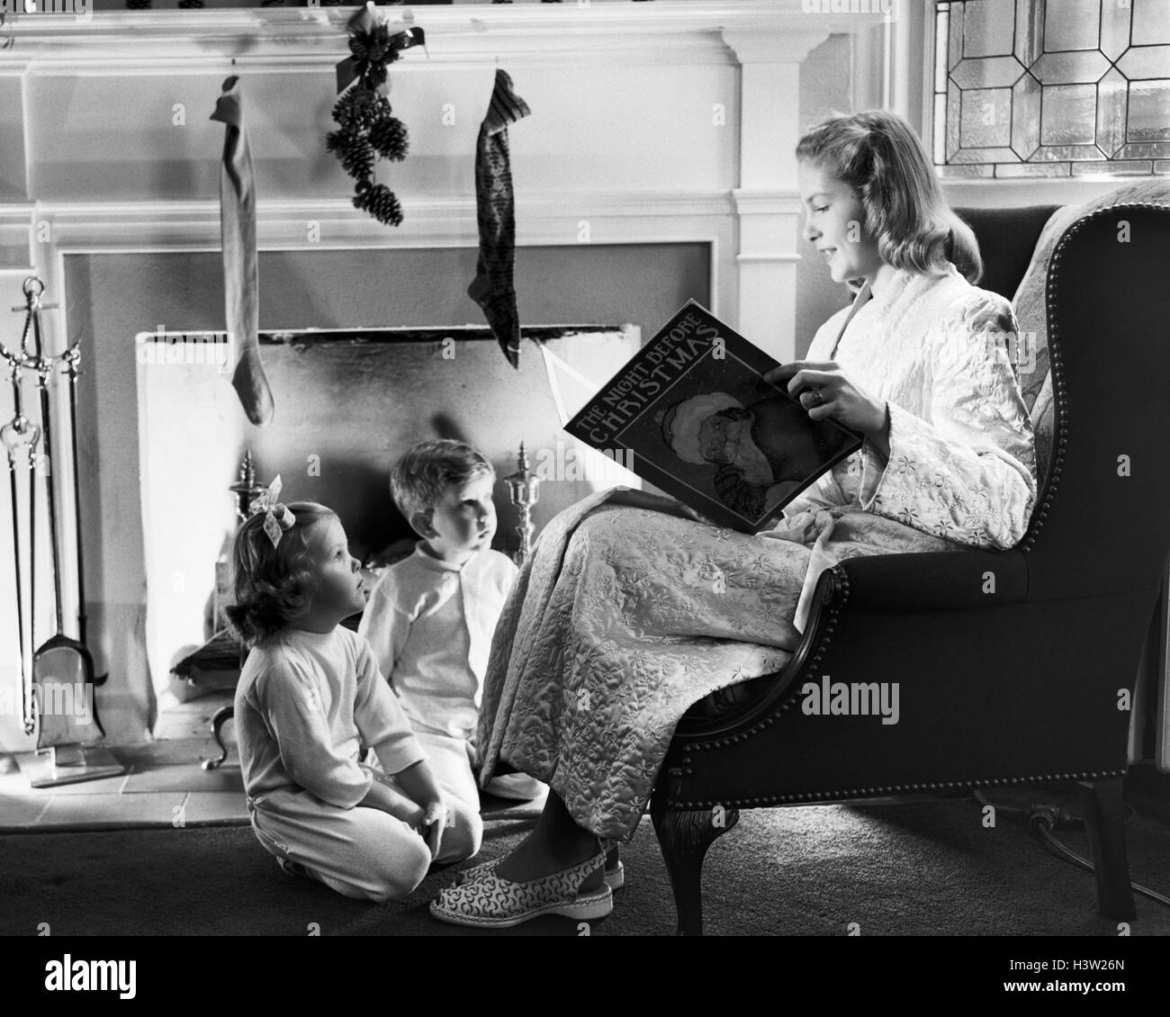 1940 1950 madre leyendo Christmas Story a chico chica sentada junto a la  chimenea con medias colgadas Fotografía de stock - Alamy