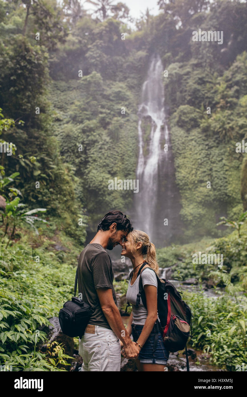 Disparo de afectuosa pareja joven de pie juntos en el bosque. Pareja de amor de pie cerca de una cascada en el bosque. Foto de stock