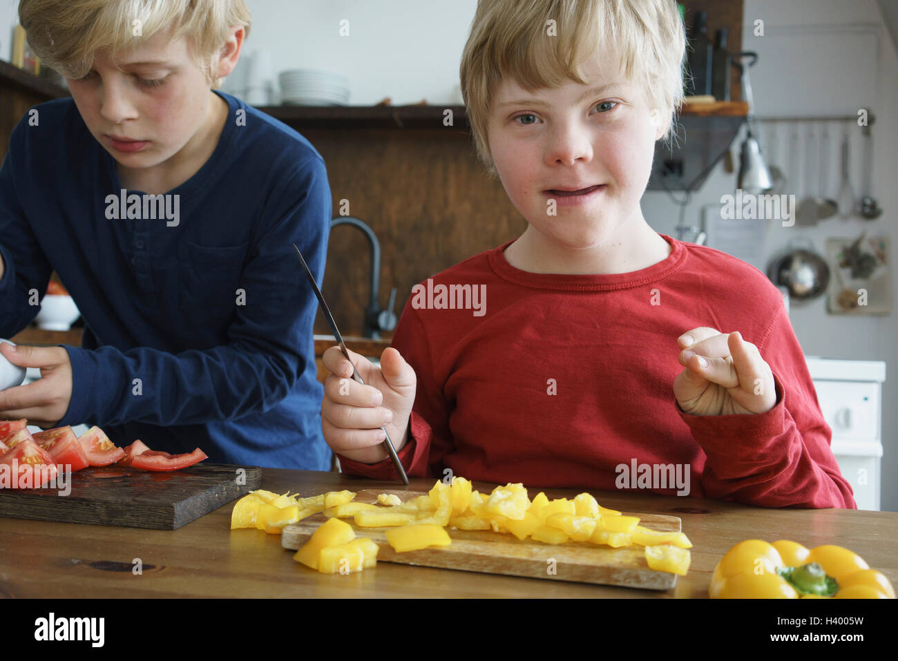 Retrato de discapacitados por el hermano muchacho sentado a la mesa con las verduras en la cocina Foto de stock