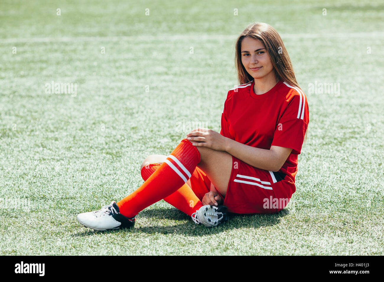 Retrato de alegre futbolista adolescente sentado en campo Foto de stock