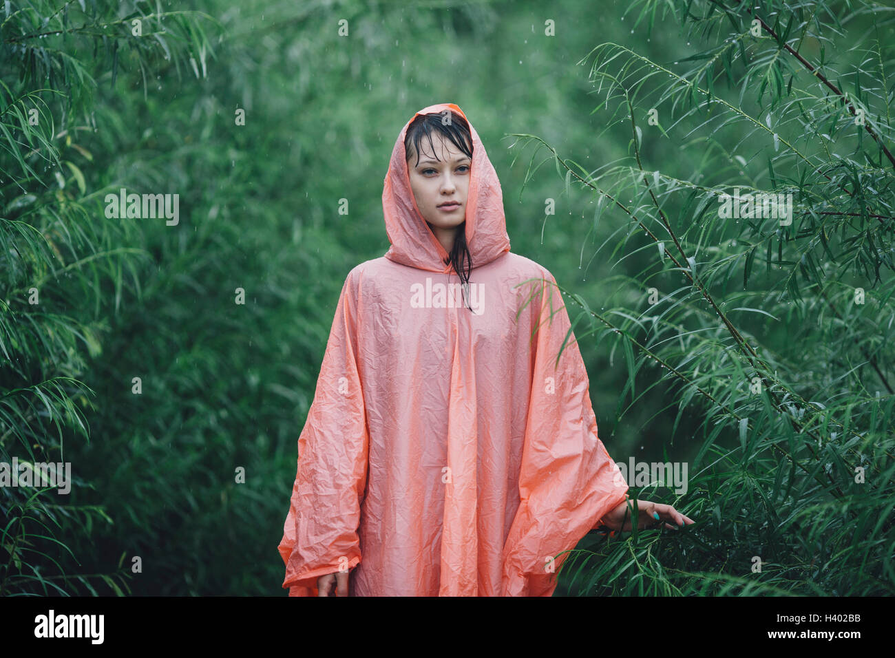 Joven mujer vistiendo impermeable de pie en medio de plantas durante la temporada de lluvias Foto de stock