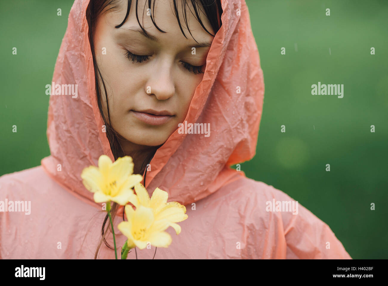Close-up de hermosa mujer vistiendo impermeable sosteniendo flores amarillas en la temporada de lluvias Foto de stock