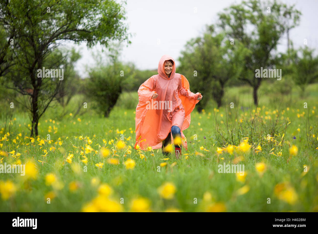 Mujer vistiendo impermeable girando en medio de las plantas con flores amarillas en la temporada de lluvias Foto de stock