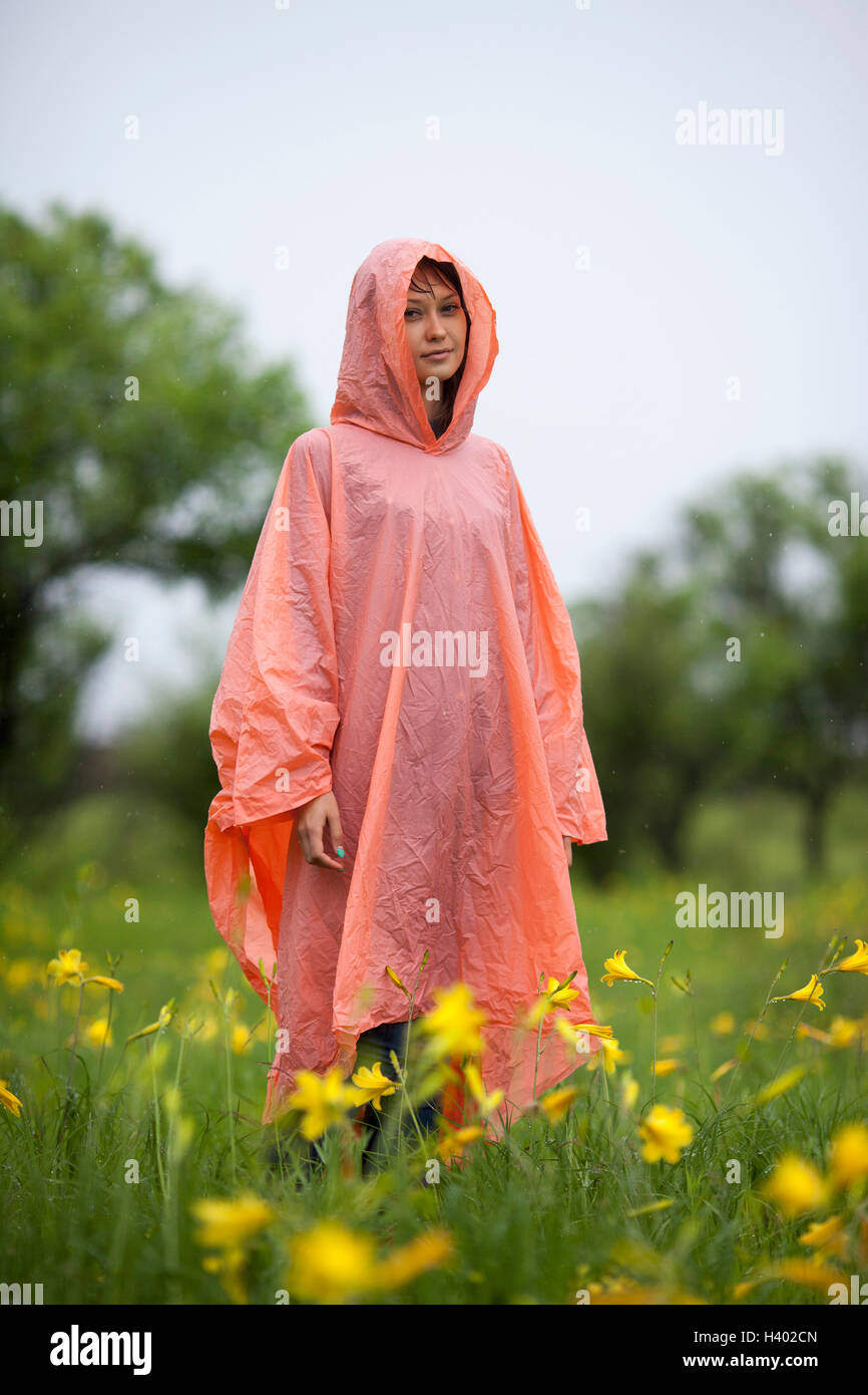 Mujer vistiendo impermeable de pie en medio de plantas de floración amarilla en la temporada de lluvias Foto de stock