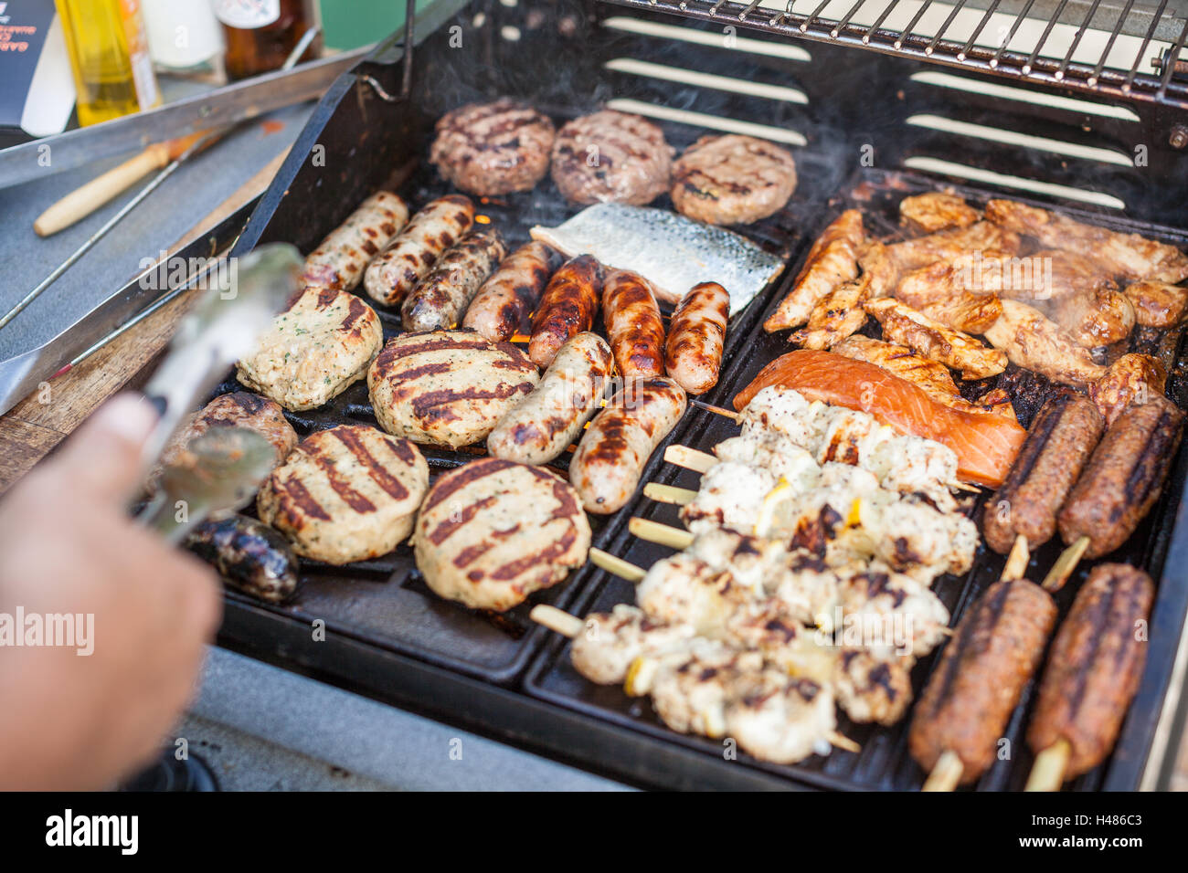 Smokey barbacoa de gas cocinar varias carnes (hamburguesas, salchichas,  pescado, cordero, carnes) en un caluroso día de sol en el jardín de atrás  Fotografía de stock - Alamy