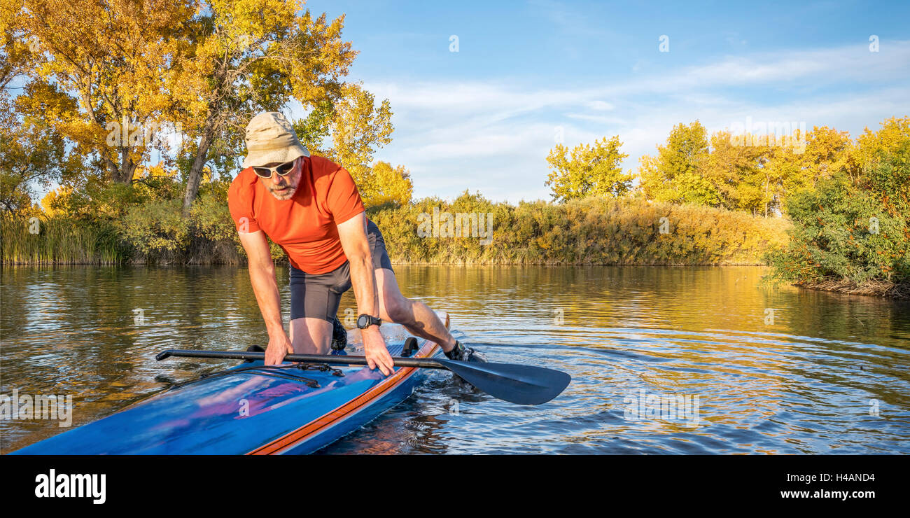 Paddler senior masculino está iniciando sesión en su stand up paddleboard racing en colores de otoño en el lago en Colorado Foto de stock