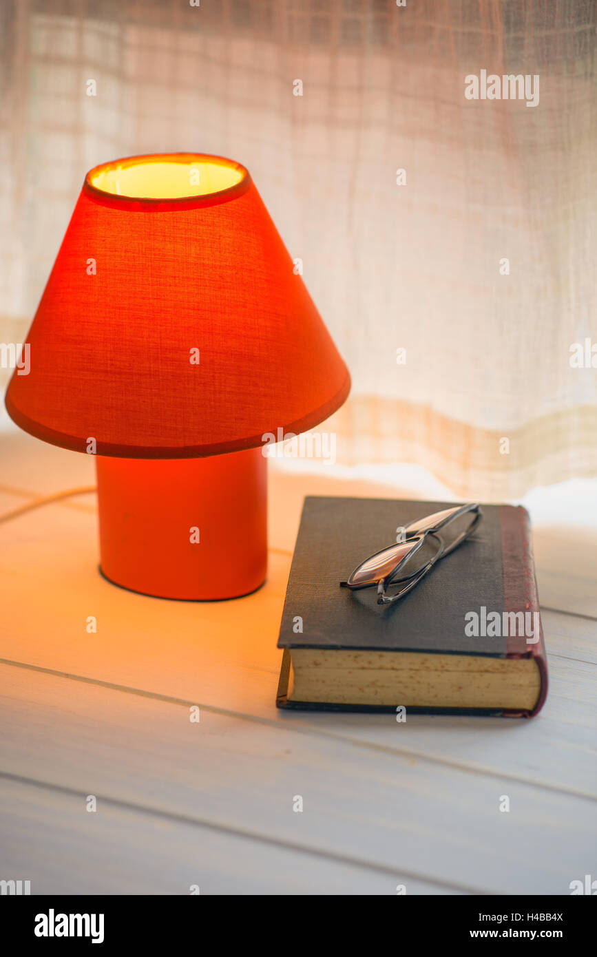 Lámpara de escritorio, libro rojo y gafas de espacio de copia de la repisa de la ventana. Foto de stock
