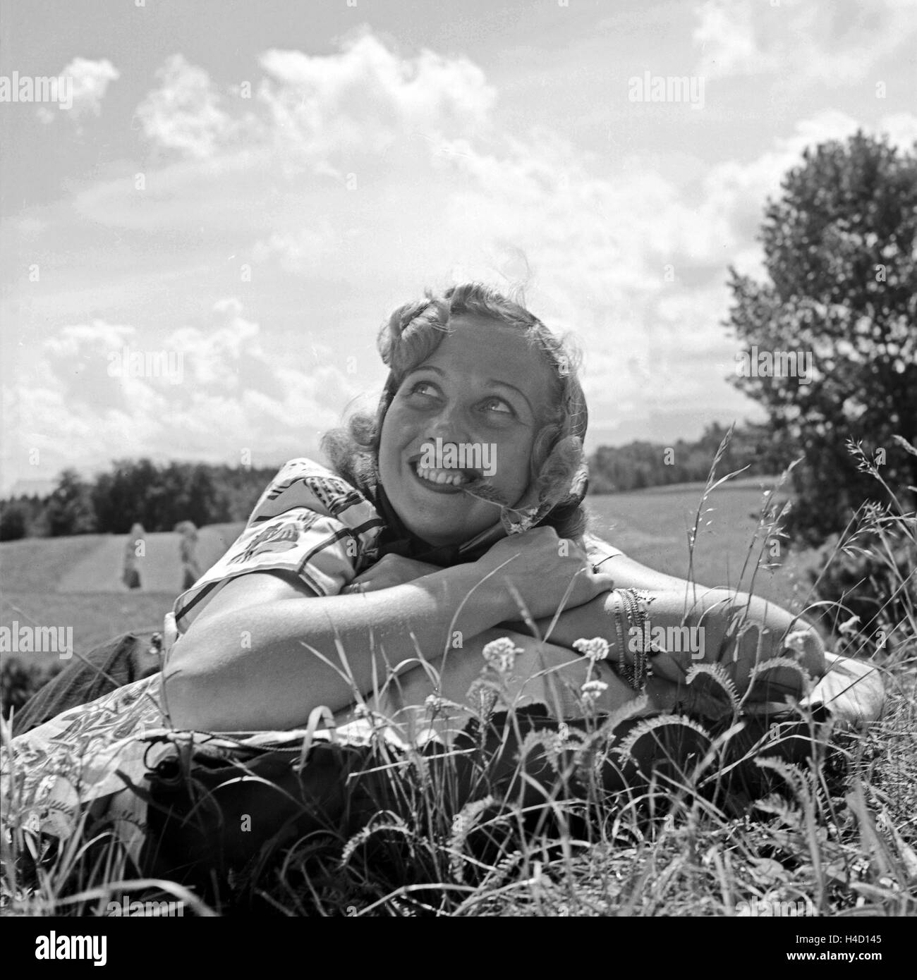 Eine junge Frau liegt lachen en einer Wiese, Deutschland 1930er Jahre. Una mujer joven acostado en el pasto, sonriente, Alemania 1930. Foto de stock