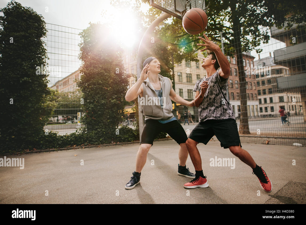 Amigos adolescentes jugando baloncesto uno contra el otro en la terraza de un tribunal. Dos hombres jóvenes jugando un partido de baloncesto. Foto de stock