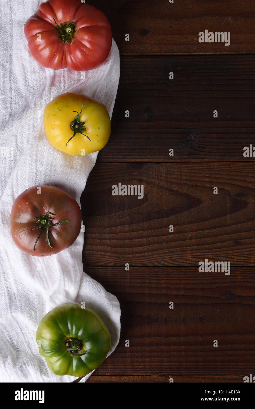 Vista superior de herencia tomates en una toalla de cocina y mesa de madera oscura. Foto de stock