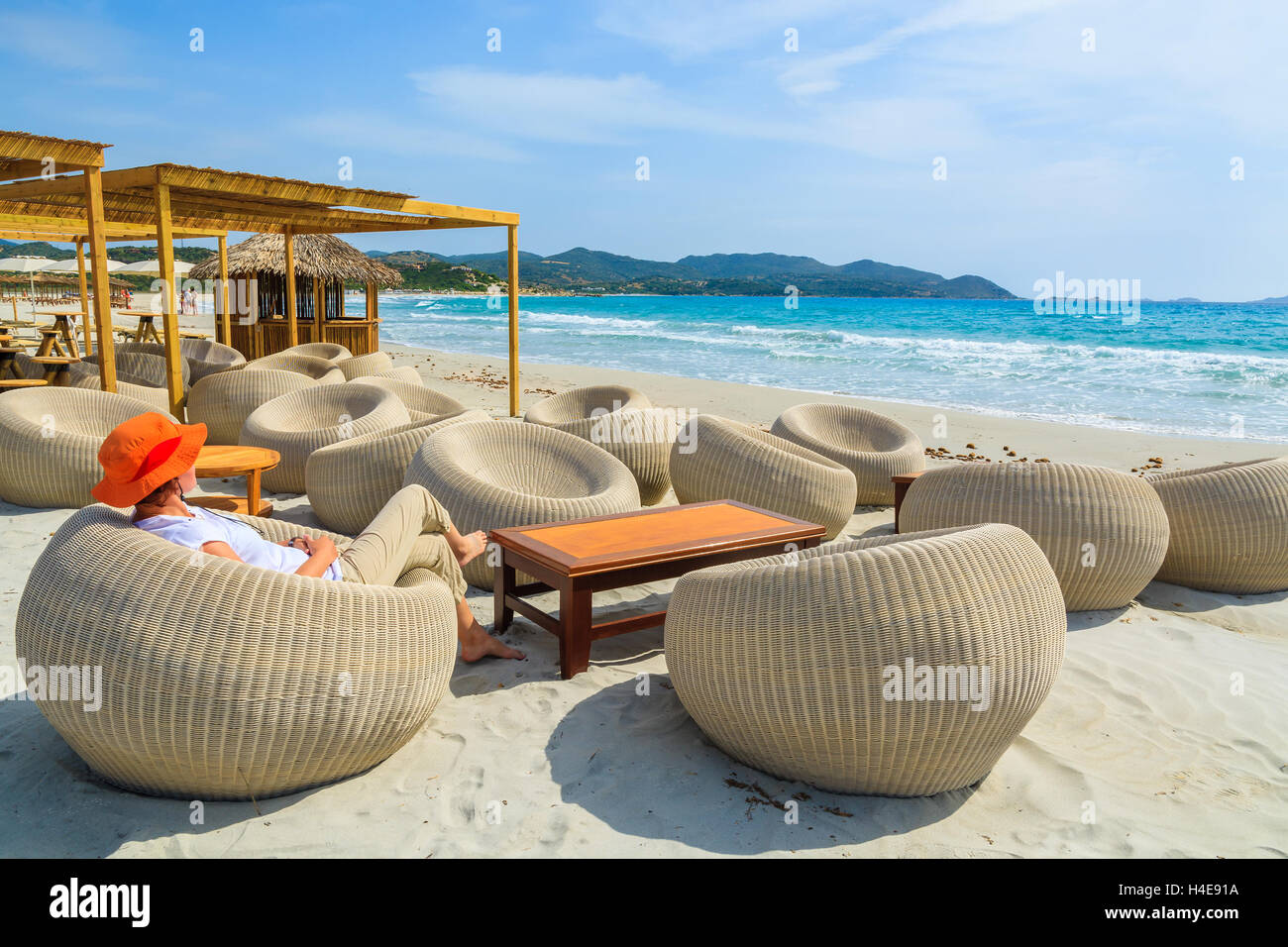 Joven turista se sienta en un bar en la playa de Porto Giunco bay, Isla Cerdeña, Italia Foto de stock