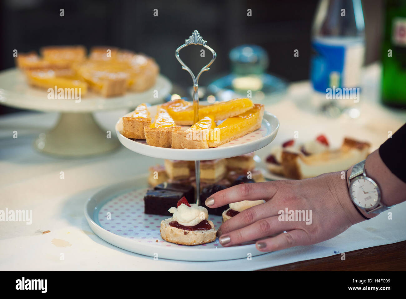 Busca deliciosas tortas en un stand de dos niveles con la mano de una persona para tomar uno Foto de stock