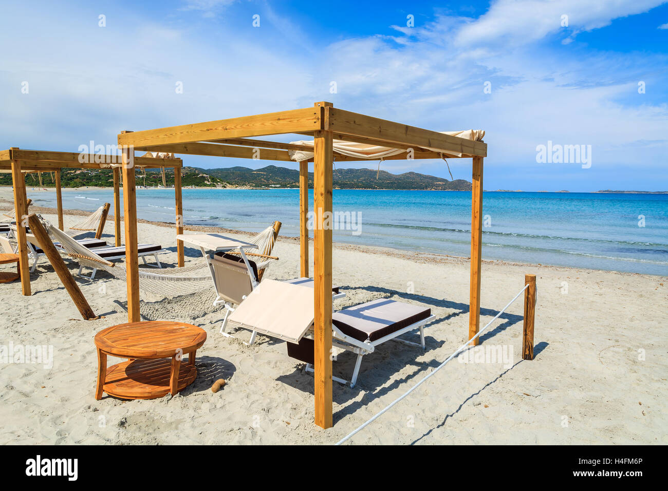 Sillas y hamacas de madera con mesa de teca en la playa de arena blanca en la bahía de Porto Giunco, Cerdeña, Italia Foto de stock