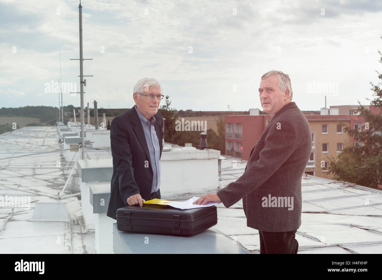 Dos altos empresarios con documentos que un acuerdo comercial al aire libre en la azotea de un edificio. Foto de stock