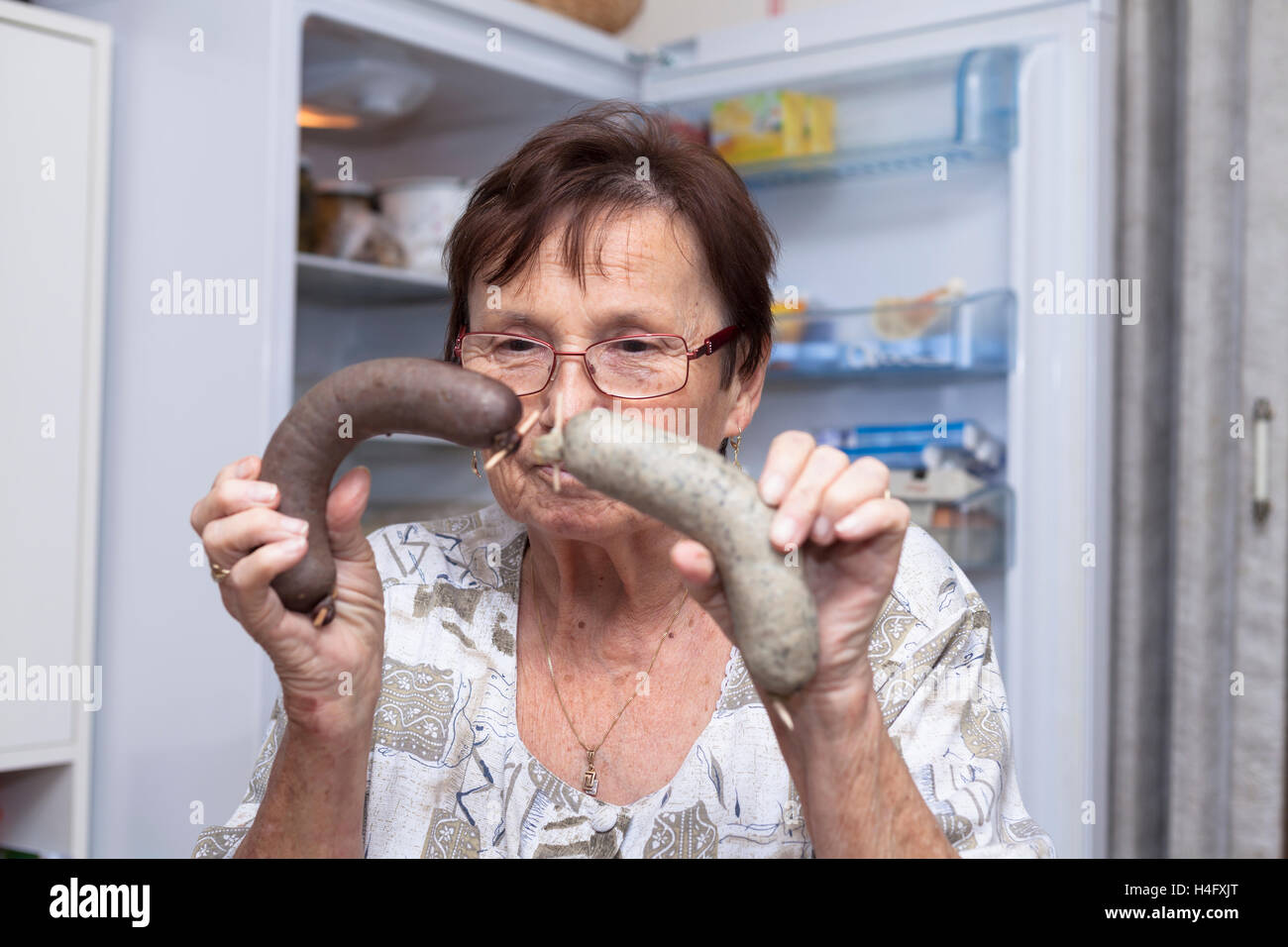 Mujer sosteniendo senior de salchichas de hígado de cerdo mientras está de pie delante de la nevera en la cocina abierta. Foto de stock