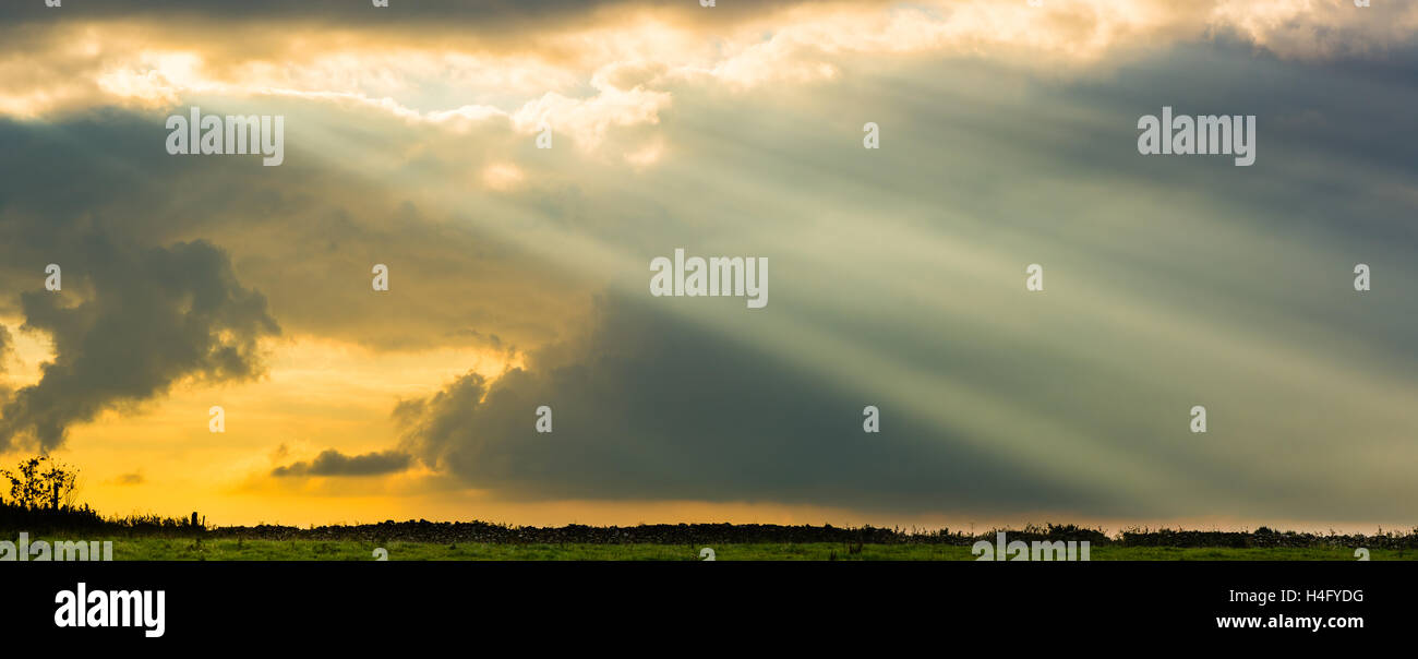 Rayos de sol entre nubes encima del campo y el muro de piedra seca. Impresionante cielo iracundo con el sol, por encima de los pastos en la campiña inglesa Foto de stock