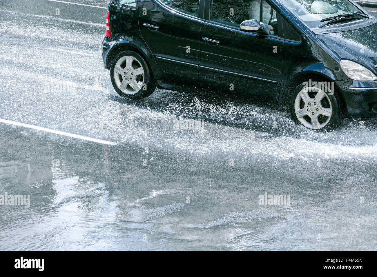 Coche de conducción en carretera inundada con agua después de la lluvia, las salpicaduras de las ruedas de coche Foto de stock