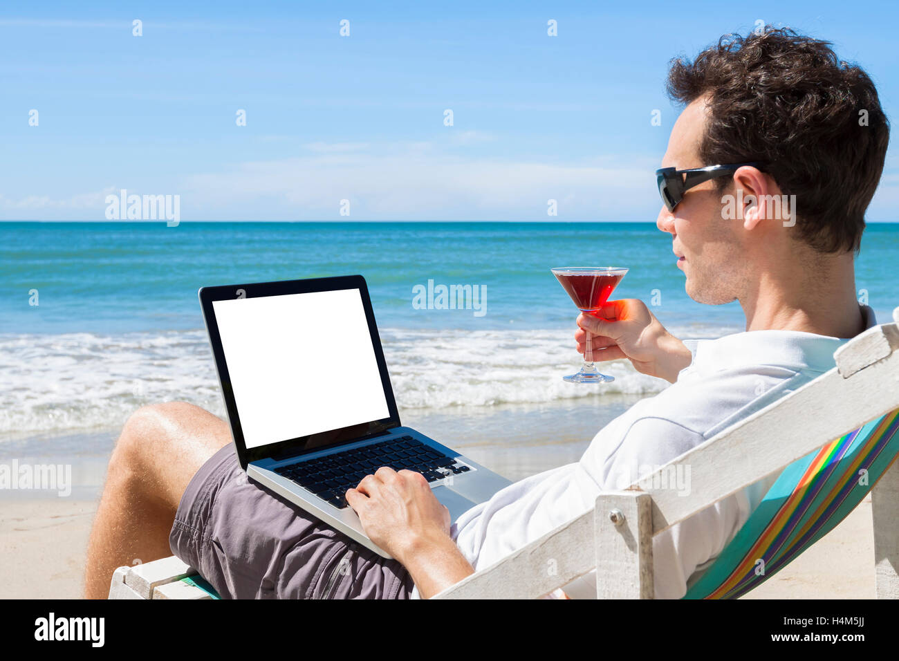Freelancer independiente escribiendo correos electrónicos sobre la playa tropical con un cóctel en la mano Foto de stock