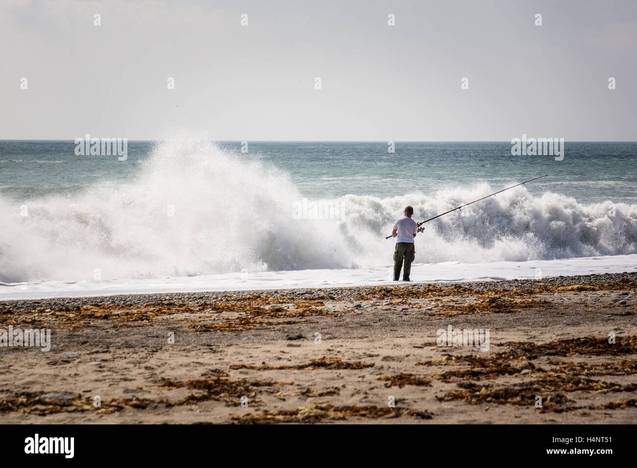 Hombre que pesca con vara en una playa con grandes olas que rompen en la orilla Foto de stock