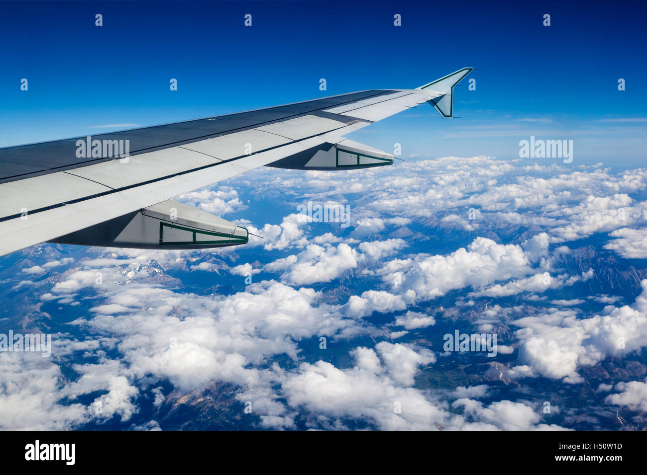Vista de la ventana del avión mostrando ala de avión que volaba sobre las nubes y montañas rocosas. Foto de stock