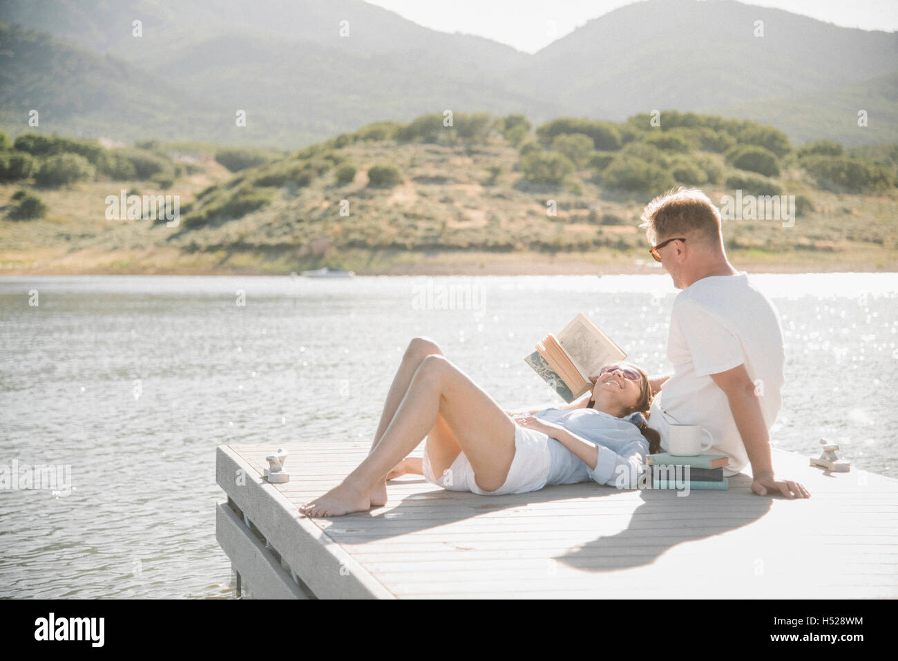 Hombre y mujer recostado sobre un embarcadero, leyendo un libro. Foto de stock