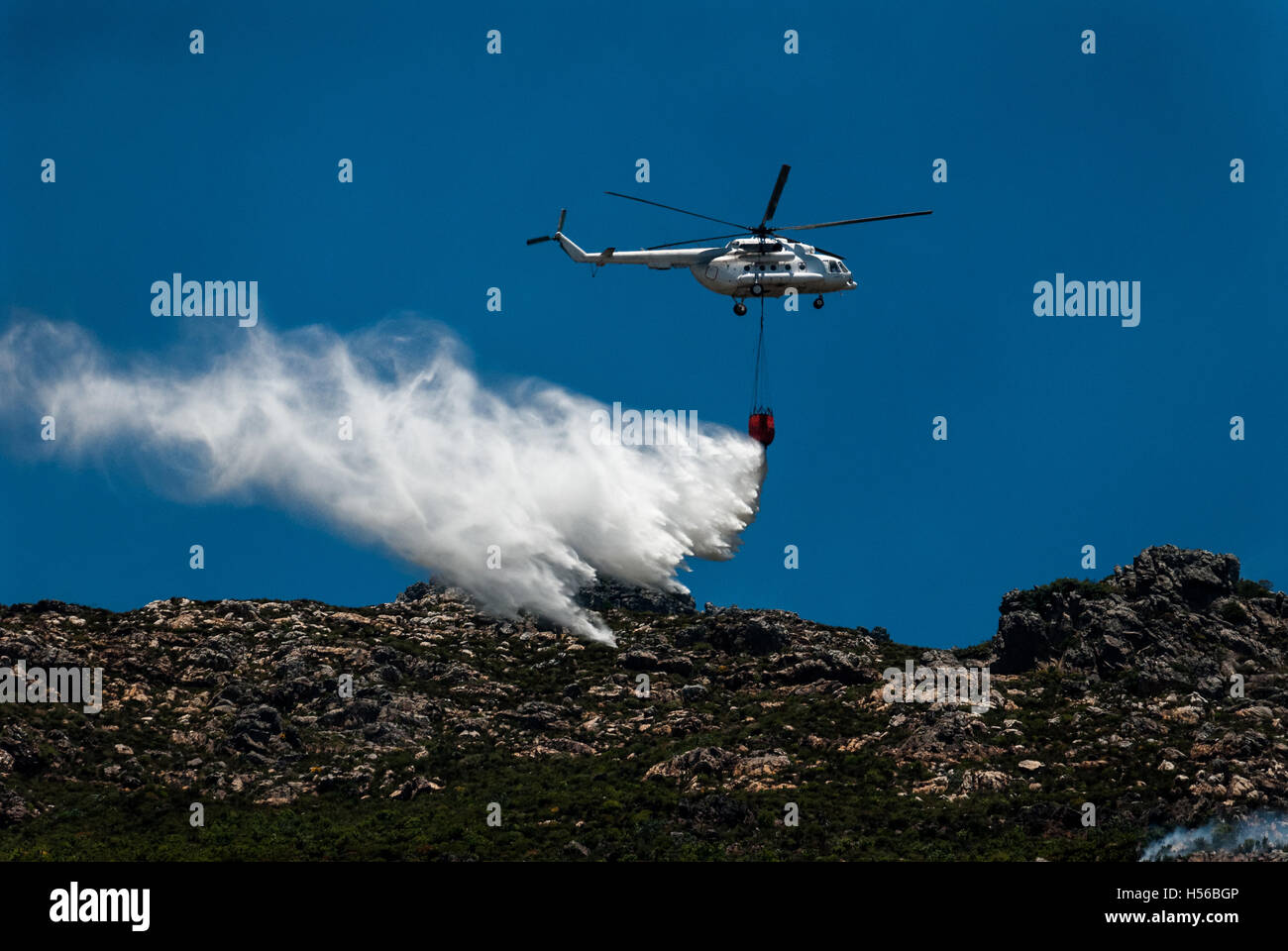 Helicóptero de lucha contra incendios que cae un gran rociador de agua desde su balde colgante sobre un fuego de montaña Foto de stock