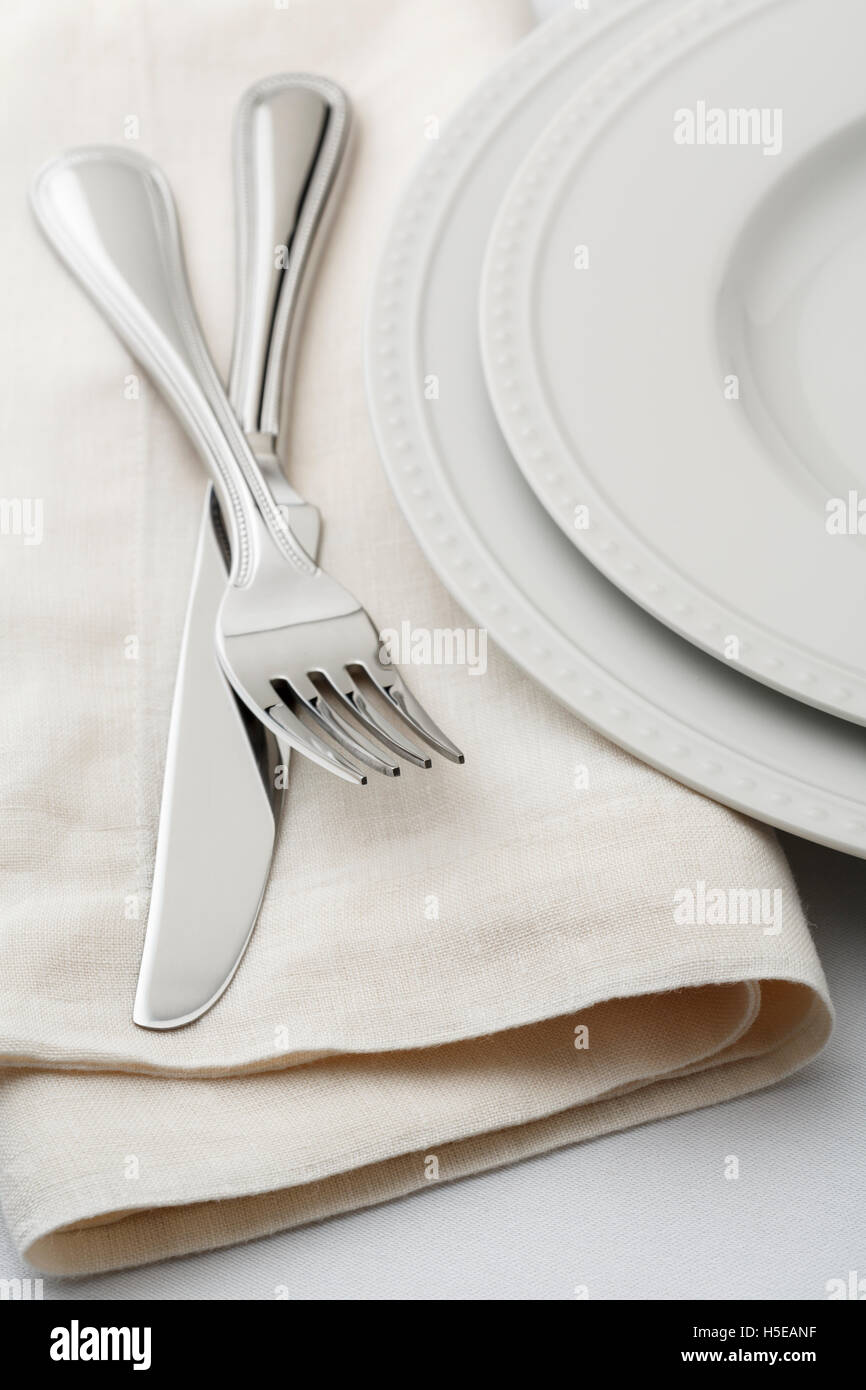Restaurantes estilo clásico ajuste table place setting con vajilla, ropa de cama blanca servilleta y platería tenedor y cuchillo. Foto de stock