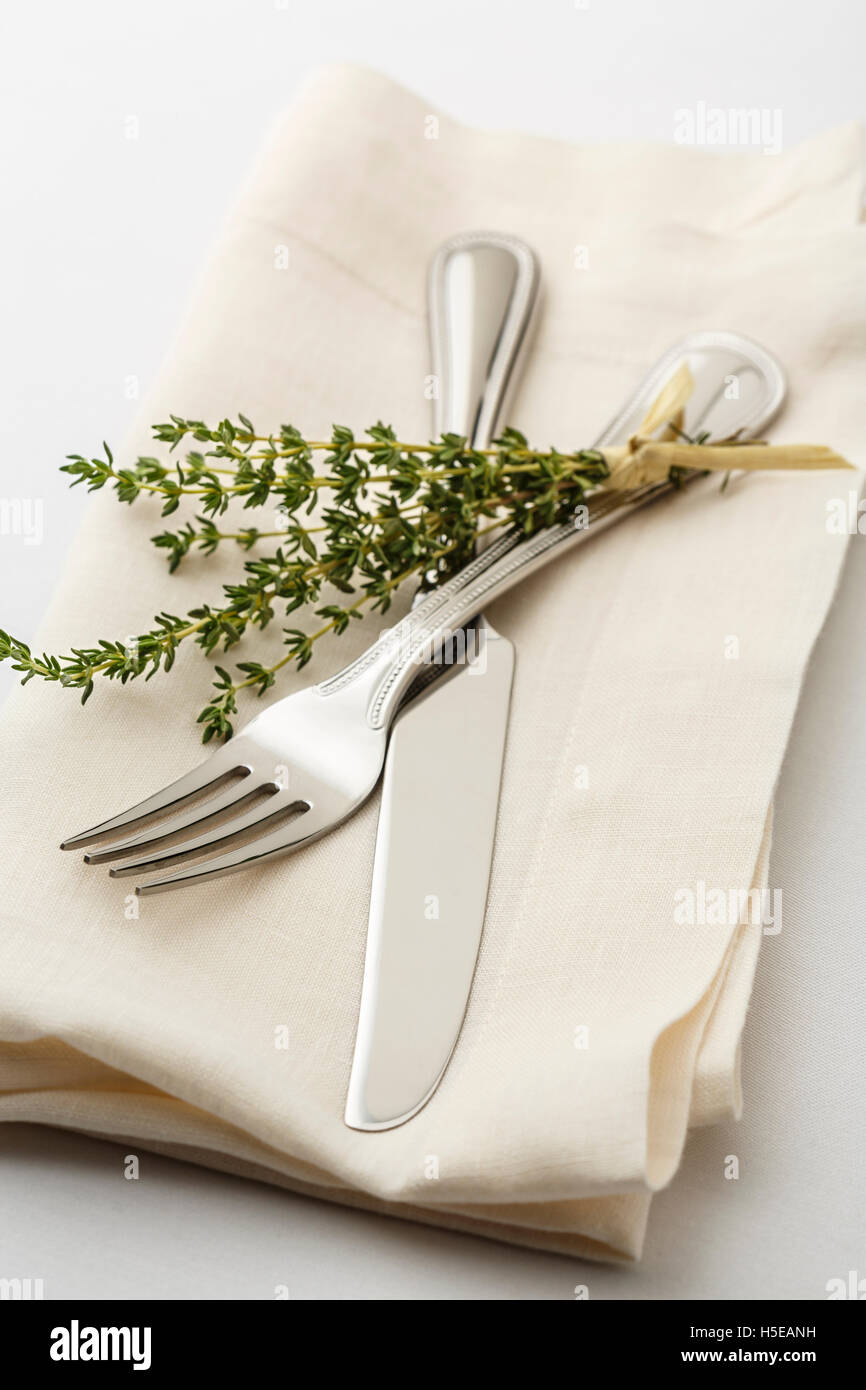 Simple, clásico lugar para poner la mesa con cubertería de plata tenedor y cuchillo en una servilleta de lino blanco y una ramita de tomillo fresco hierbas Foto de stock