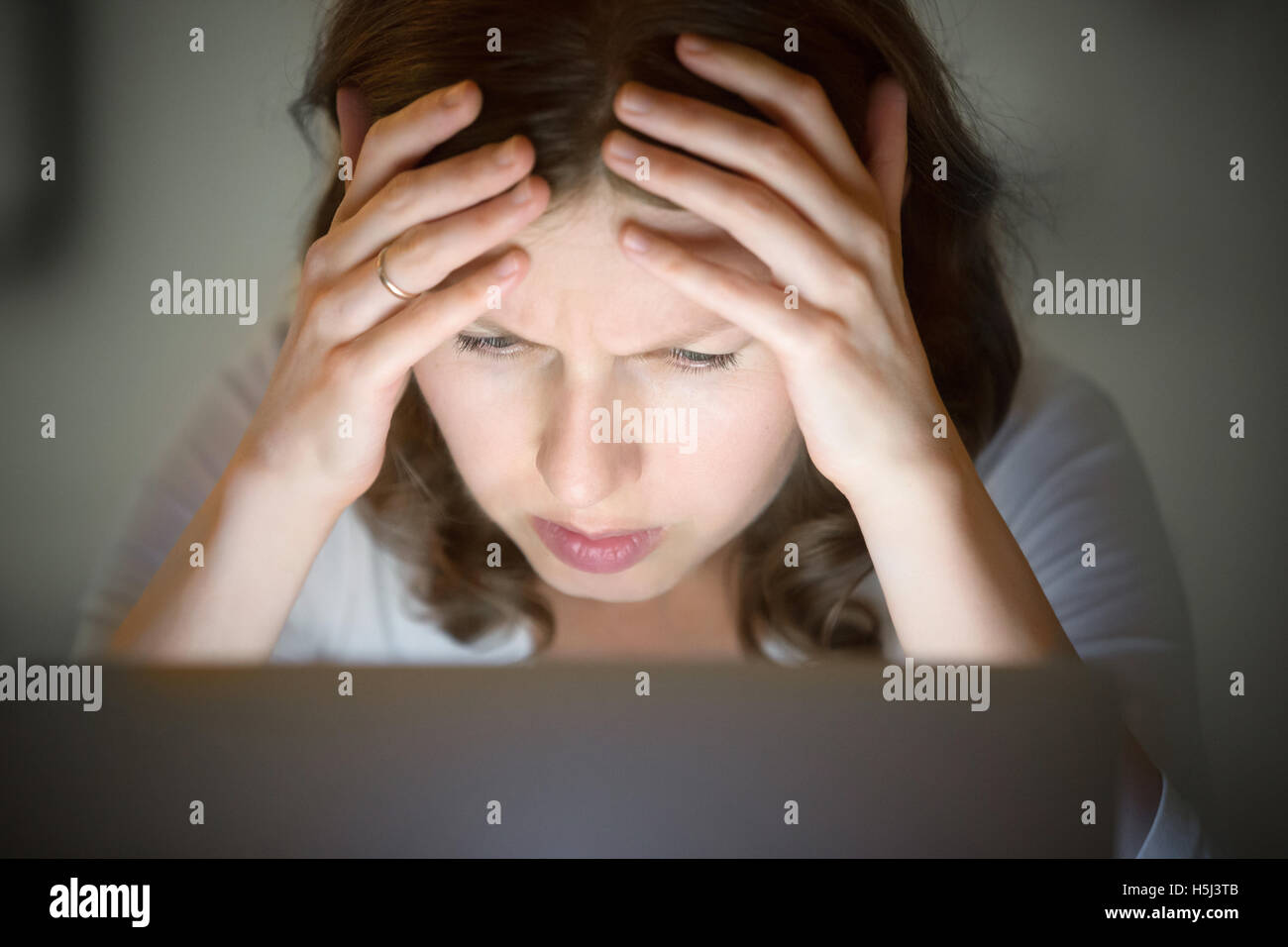 Retrato de una mujer agarrando la cabeza cerca de laptop, tarde en la noche Foto de stock