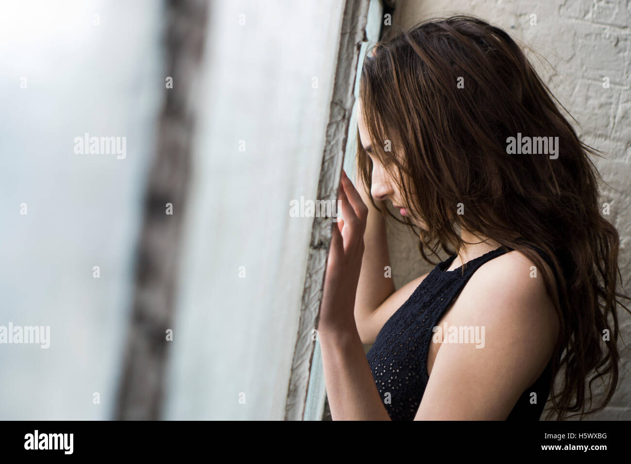 Triste joven de pie junto a la ventana Foto de stock