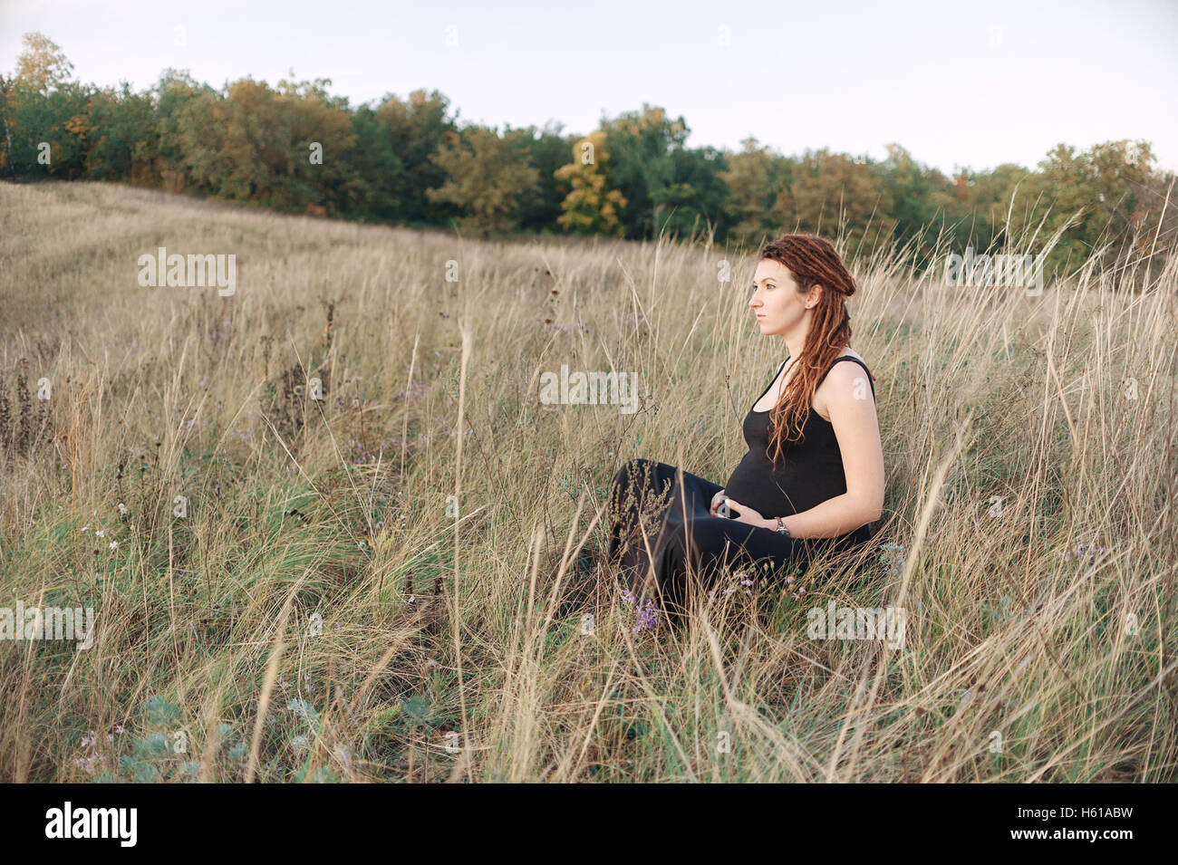 Mujer embarazada en vestido negro y dreadlocks en el fondo de la naturaleza salvaje Foto de stock