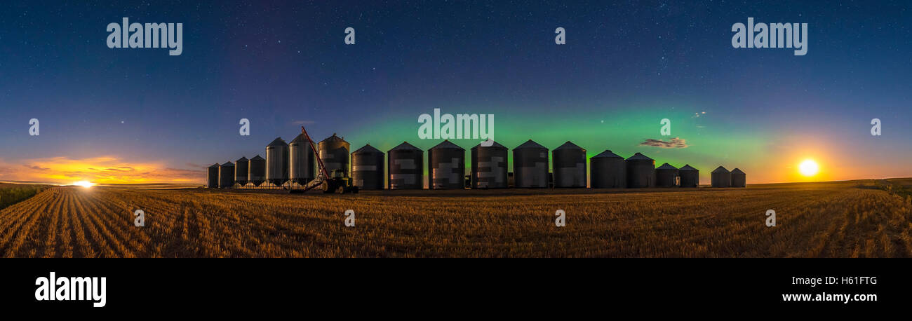 Un tenue aurora resplandeciente durante la cosecha en curso esta noche, con camiones y combina la iluminación del campo de la izquierda, y la Har Foto de stock