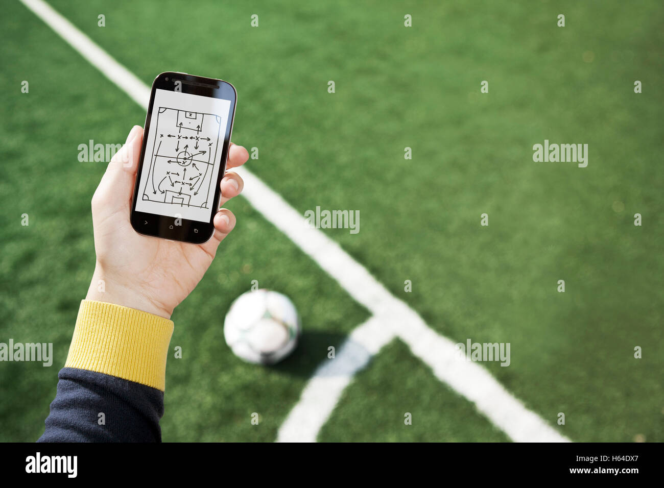 Mano sujetando smart phone con match tácticas en campo de fútbol Foto de stock