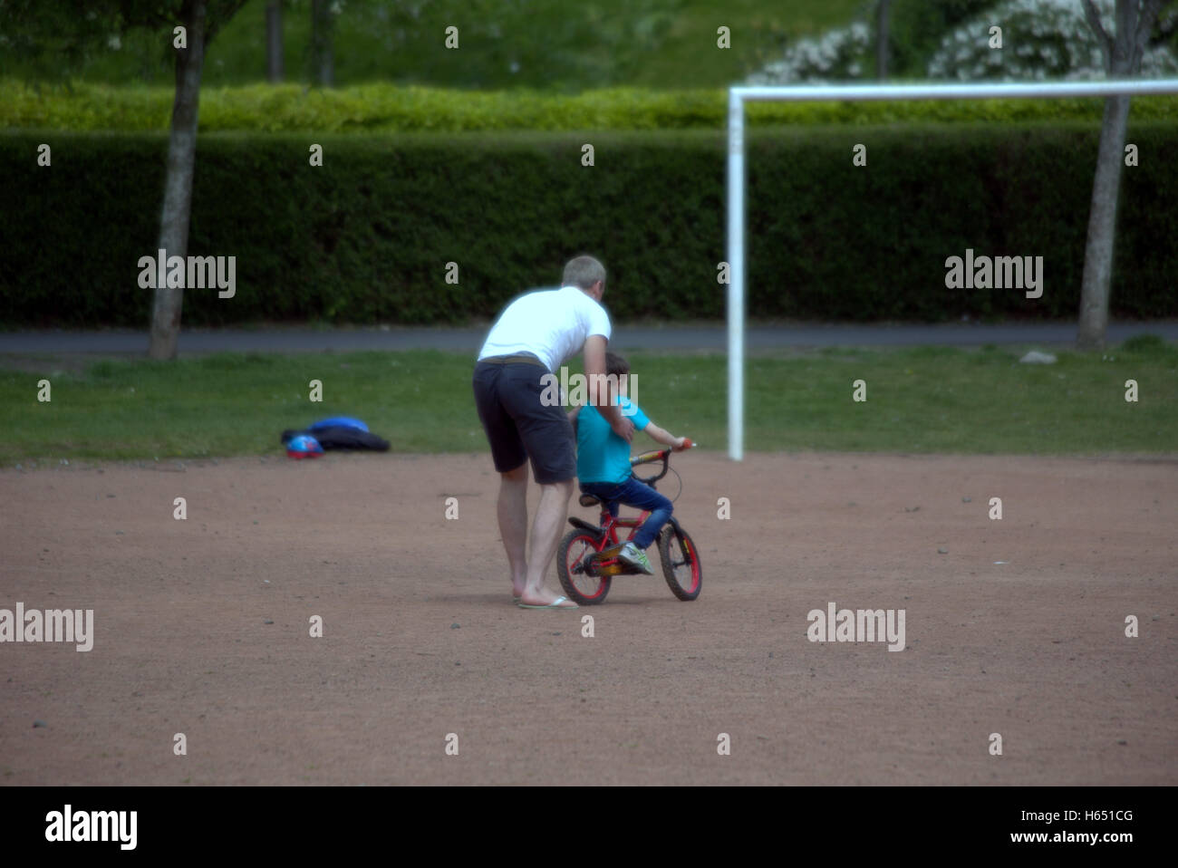 Padre enseña al hijo a correr en bicicleta con el objetivo claramente delante de él Foto de stock