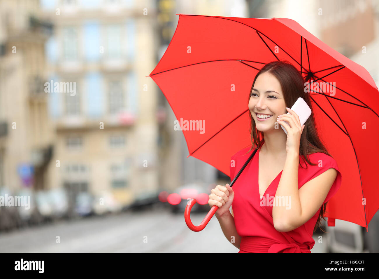 Feliz la mujer en rojo hablando por un teléfono inteligente bajo una sombrilla en la calle de una ciudad vieja Foto de stock