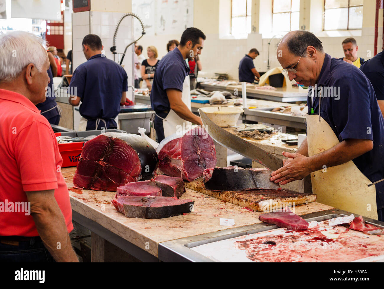 Un pez monger corta rebanadas de atún pescado con un machete, un cuchillo en la sala de mercado de Funchal en la isla portuguesa de Madeira. Foto de stock