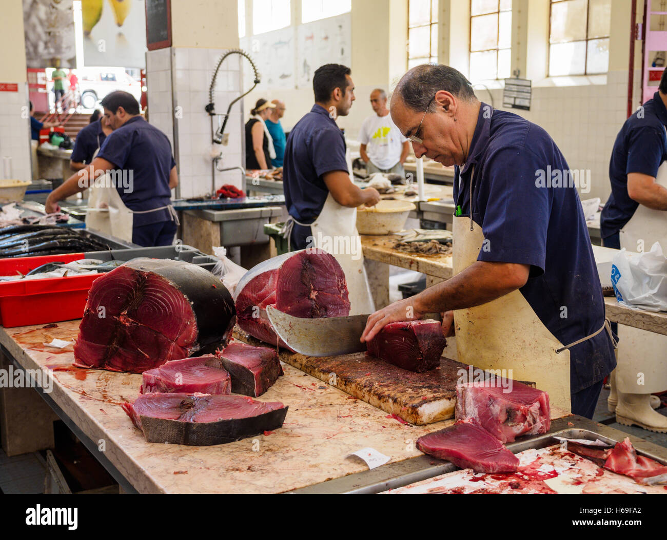 Un pez monger corta rebanadas de atún pescado con un machete, un cuchillo en la sala de mercado de Funchal en la isla portuguesa de Madeira. Foto de stock