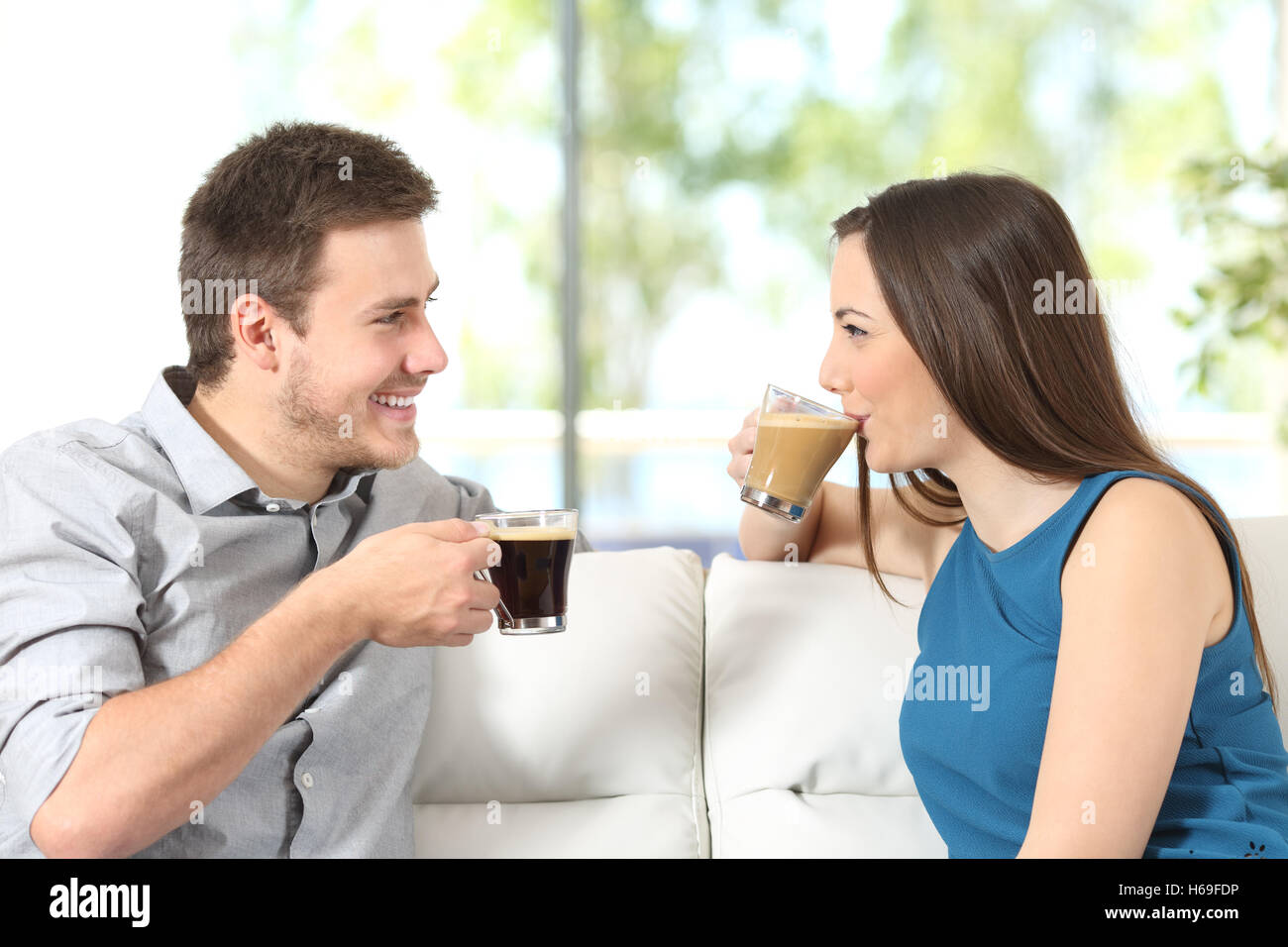 Vista lateral retrato de una pareja feliz mirando el uno al otro hablando y bebiendo café sentado en un sofá en casa Foto de stock